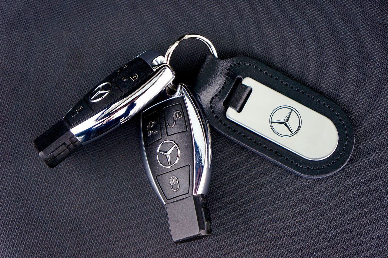 Close-up of Mercedes-Benz car keys with a leather keychain on dark fabric background.